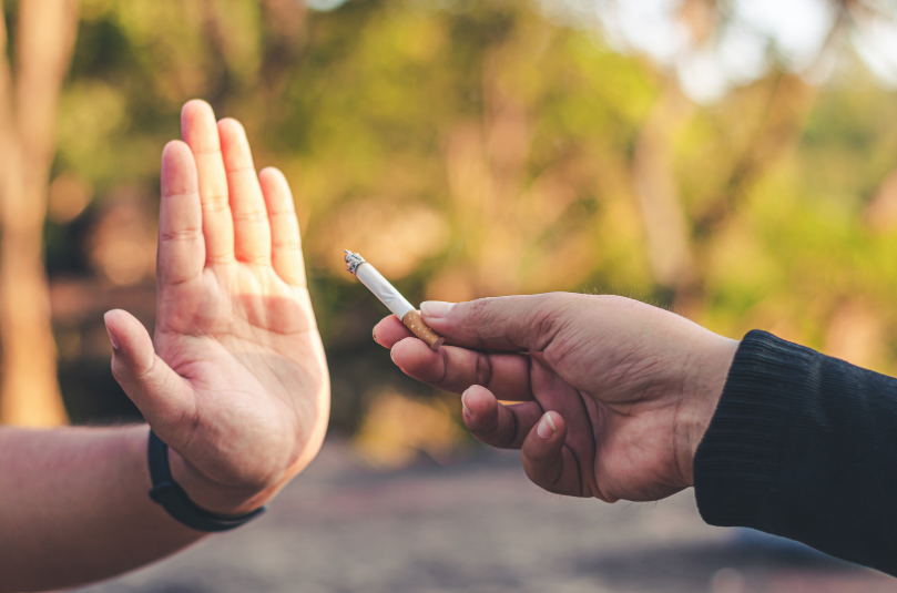 Hand offering a lit cigarette to someone who is holding out their hand as a rejection